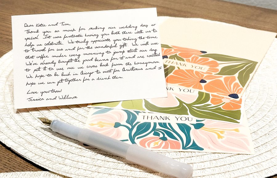 A thank-you note written out in cursive on a cream card, beside a fountain pen and two floral thank-you cards.